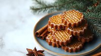 Honey waffle cookies with cinnamon sticks and star anise on blue ceramic plate near pine branches. Cozy winter holiday baking and festive treats.
