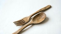 Rustic wooden fork and spoon set on white textured surface, showcasing natural grain and handcrafted charm for kitchen and food styling.