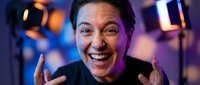 Excited Asian woman laughing with hands raised in celebration at modern restaurant or bar with colorful neon lighting and bokeh background atmosphere.