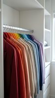 Organized walk-in closet with colorful clothes arranged by rainbow spectrum on hanging rod in modern white wardrobe storage system for home organization.