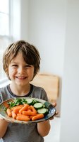 Happy young boy holding plate of fresh vegetables carrots cucumbers parsley in bright kitchen promoting healthy eating habits and nutritious lifestyle.