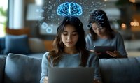 Young Asian woman working on laptop with glowing digital brain and data visualization elements floating above, colleague in background using tablet.