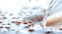 Macro photography of water drops on textured surface with dynamic splash and ripple effect creating abstract pattern in soft beige and white tones.
