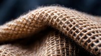 Close-up of natural burlap fabric showing textured weave pattern and fibers against dark background, useful for rustic design projects.