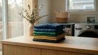 Stack of neatly folded colorful clothes on wooden surface in bright modern laundry room with natural sunlight streaming through window.