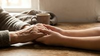 Elderly hands gently holding young hands in warm sunlight, showing intergenerational love, care and family support in cozy home setting.