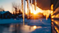 Glowing icicles hanging against winter sunset with sun rays creating magical bokeh effect in snowy landscape, dramatic nature photography with warm and cold tones.