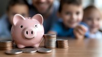 Pink ceramic piggy bank with stacked coins on wooden table, symbolizing family savings, financial education and money management for children.