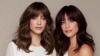 Two women with trendy curtain bangs and layered hairstyles showcase modern haircuts - brunette and dark brown shades styled in loose waves against neutral background.