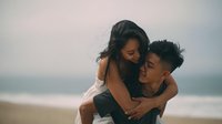 Young Asian couple embracing on beach at sunset, romantic moment with ocean waves in background, love and relationship concept for lifestyle content.