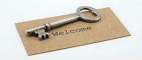Vintage metal key resting on a kraft paper card with Welcome text, symbolizing new home, hospitality, and real estate concepts.