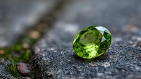 Brilliant cut peridot gemstone on dark textured surface, showcasing vibrant green color and facets for jewelry design and luxury concepts.