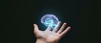 Glowing digital brain hologram floating above open palm against dark background representing artificial intelligence, neuroscience and mental health concepts.