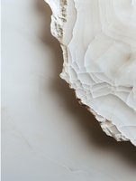 Close-up view of white alabaster or onyx stone with natural layered texture and rough edges against neutral background, showcasing mineral formation patterns.