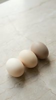 Three fresh chicken eggs in different shades from white to brown arranged on marble surface for cooking and baking recipes.