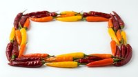 Colorful hot chili peppers arranged in rectangular frame border with red, orange and yellow varieties on white background, suitable for food and cooking content.