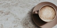 Creamy cappuccino with foam in elegant brown ceramic cup and saucer on marble surface, perfect for cafe menus and coffee shop branding materials.