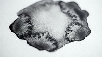 Abstract black ink blot with white center on paper surface. Organic fluid shape resembling Rorschach test pattern for psychology, creativity and artistic projects.