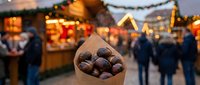 Roasted chestnuts in paper cone at festive Christmas market with warm lights and wooden stalls creating cozy winter atmosphere for holiday celebrations.