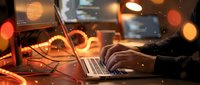 Professional working late at night on laptop with warm ambient lighting and bokeh effects creating productive workspace atmosphere.