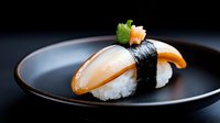 Fresh nigiri sushi with raw fish and nori on black ceramic plate against dark background, close up view of traditional Japanese cuisine served in restaurant.