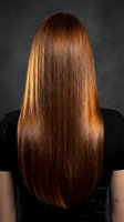 Woman with long straight glossy auburn hair viewed from behind, showcasing a salon keratin treatment result on dark background.