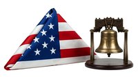 Folded American flag with stars and stripes next to brass liberty bell on wooden stand, patriotic symbols for independence day celebrations and historical commemorations.