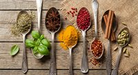 Colorful spices and herbs arranged in vintage spoons on rustic wooden background with fresh basil leaves and burlap texture for culinary cooking designs.