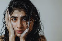 Dramatic beauty portrait of young South Asian woman with wet dark hair and natural makeup against neutral background, perfect for cosmetic and haircare advertising.