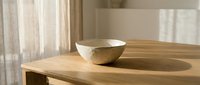 Minimalist ceramic bowl on wooden table in bright modern interior with natural sunlight creating soft shadows and warm atmosphere for home decor concepts.