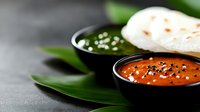 Traditional Indian chutneys in black bowls with fresh naan bread and curry leaves on dark surface for authentic cuisine and cooking concepts.