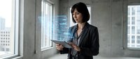 Woman professional holding tablet in modern office with city skyline view through windows, wearing business casual attire for corporate workplace concepts.