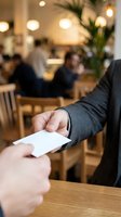 Person handing a card in a modern cafe, close-up of hands exchanging business card or payment in stylish restaurant interior.