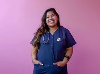 Asian female healthcare worker in navy blue scrubs and stethoscope smiling confidently against pink background, representing medical profession and diversity.
