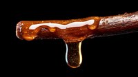 Dripping golden honey from wooden dipper against black background, macro photography showing viscous texture and natural sweetness in dramatic lighting.