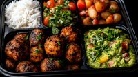 Spicy meatballs with rice, roasted vegetables and fresh green salad in black meal prep container. Healthy portioned food for weekly planning.