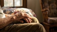 Elderly man's weathered hands resting peacefully on blanket in warm sunlit room. Senior care, aging, comfort, relaxation, golden hour lighting concept.