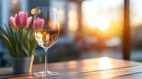 Glass of rose wine on wooden table with pink tulips and warm sunset light through window creates romantic spring atmosphere for dining and celebration.