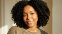 Young African American woman with natural curly afro hair smiling warmly in cozy brown sweater, portrait shot with soft lighting for lifestyle content.