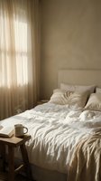 Cozy unmade bed with white linen bedding and coffee cup in warm sunlit bedroom with sheer curtains creating peaceful morning atmosphere for relaxation.
