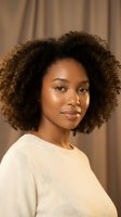 Young African American woman with natural curly afro hair wearing cream sweater looking at camera with confident expression against neutral background.