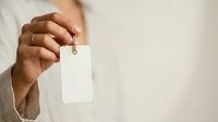 Person with medium skin tone holding blank white ID badge or name tag with lanyard for corporate branding and identification purposes.