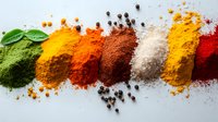 Colorful aromatic spices and herbs in powder form arranged in line with peppercorns and fresh basil leaf on white background, culinary seasoning variety.