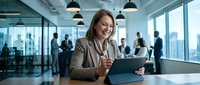 Professional businesswoman using tablet in modern office workspace with team meeting in background for corporate communication and digital workflow.