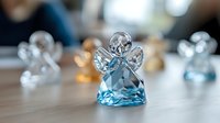 Crystal angel figurine with blue gemstone base on wooden surface, soft bokeh background creates ethereal atmosphere for spiritual and decorative concepts.