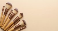 Professional makeup brushes with wooden handles arranged on beige background for cosmetic application and beauty routine.