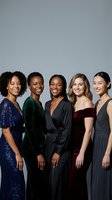 Five diverse women in elegant evening gowns standing together smiling, representing friendship, celebration and formal fashion for special occasions.