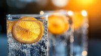 Refreshing sparkling water with orange slice in glass at sunset, bubbles rising through transparent liquid against warm golden light.