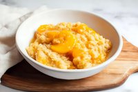 Creamy rice pudding topped with fresh peach slices in white ceramic bowl on wooden board, comfort food dessert with golden fruit garnish.