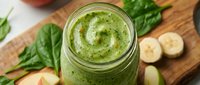 Fresh green smoothie with spinach and banana in glass jar on wooden cutting board for healthy breakfast nutrition.